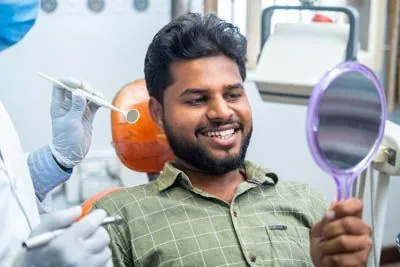 man looking in the mirror after getting dental implants at Smiles on Elston
